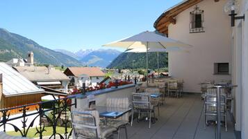 Una terrazza all'aperto con tavoli e sedie, un ombrellone grande e vista sulle montagne.
