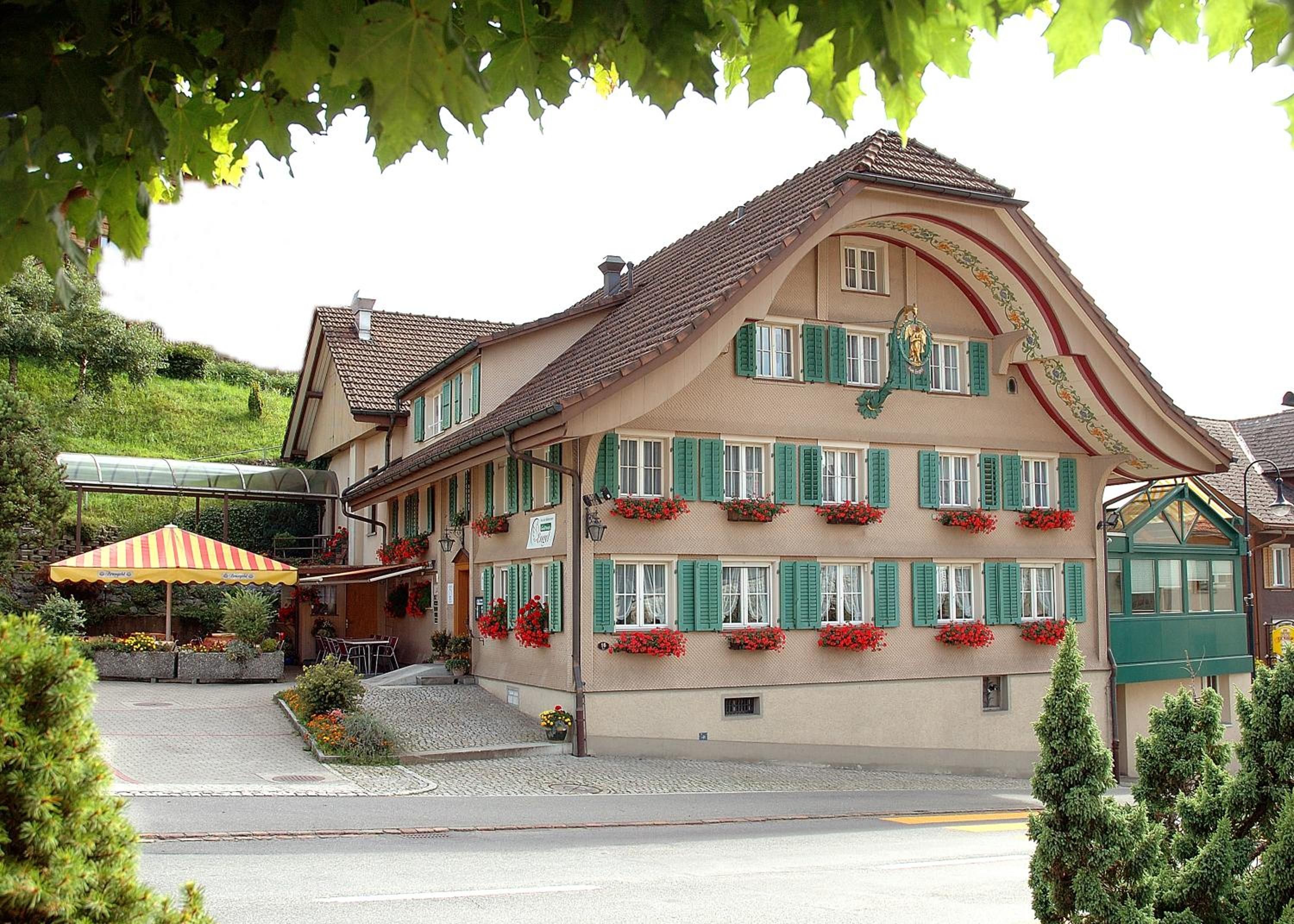 A traditional multi-story building with green shutters, a sloped roof, and flower boxes on the windows.
