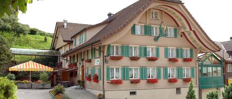 A traditional multi-story building with green shutters, a sloped roof, and flower boxes on the windows.