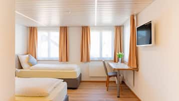 A hotel room with two beds, a desk, a chair, a TV, and windows with curtains.
