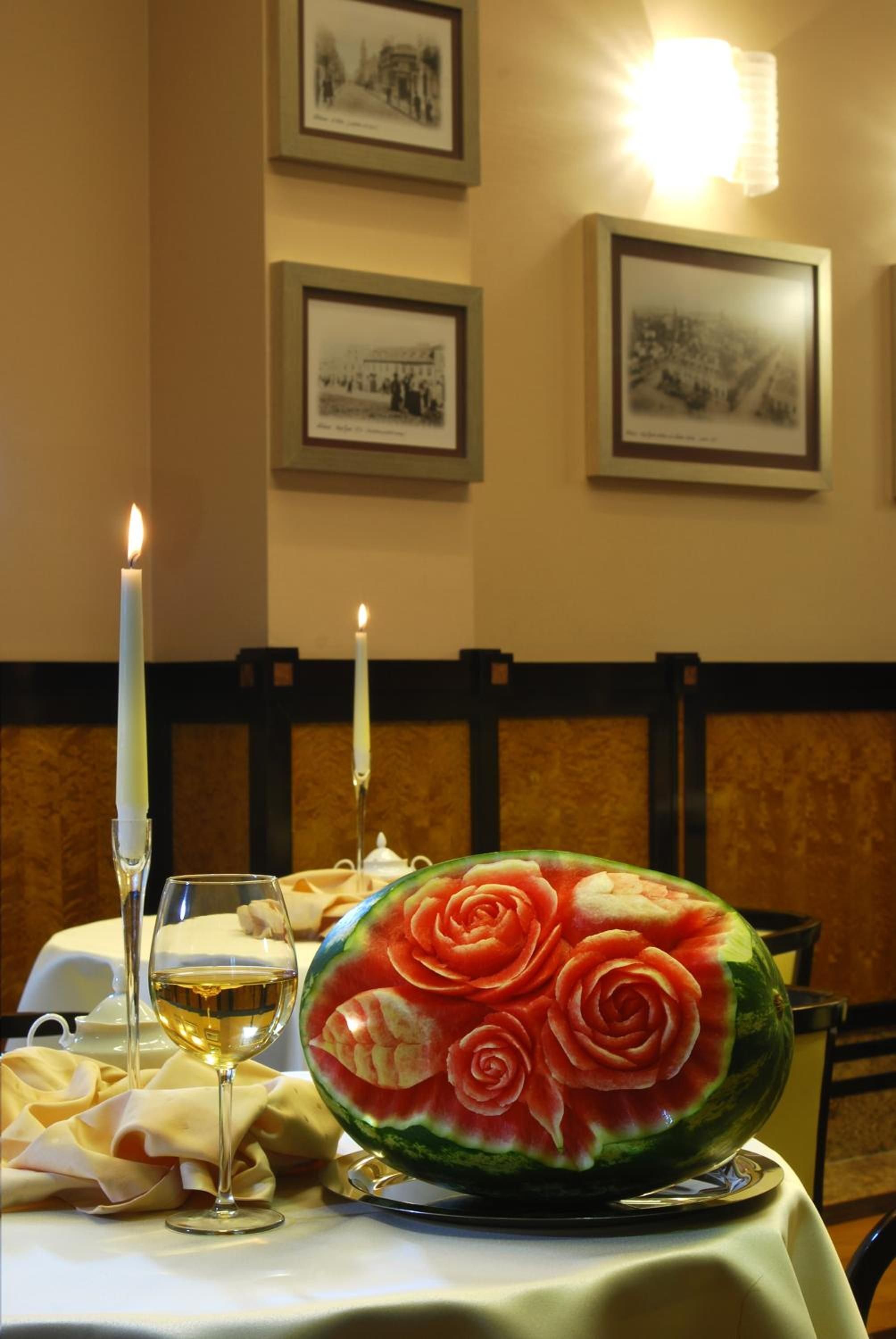 A dining table with a candle, a glass of wine, and a watermelon carved into a rose.