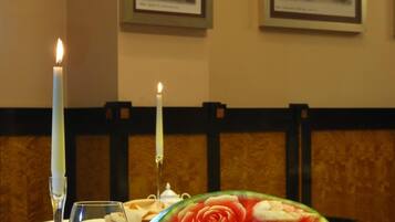 A dining table with a candle, a glass of wine, and a watermelon carved into a rose.
