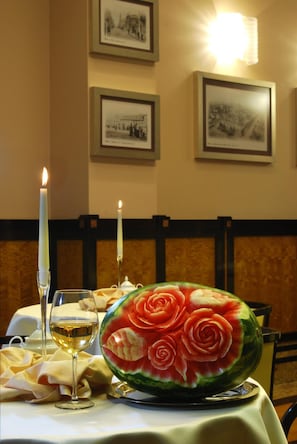 A dining table with a candle, a glass of wine, and a watermelon carved into a rose.