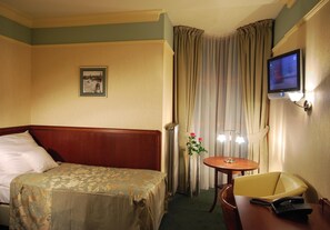 Une chambre d’hôtel avec un lit, un bureau et une chaise, une télévision et une fenêtre avec des rideaux.