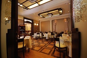 A dining area with multiple tables and chairs, a patterned floor, and a decorative ceiling. - Hotel Victoria (Wloclawek)