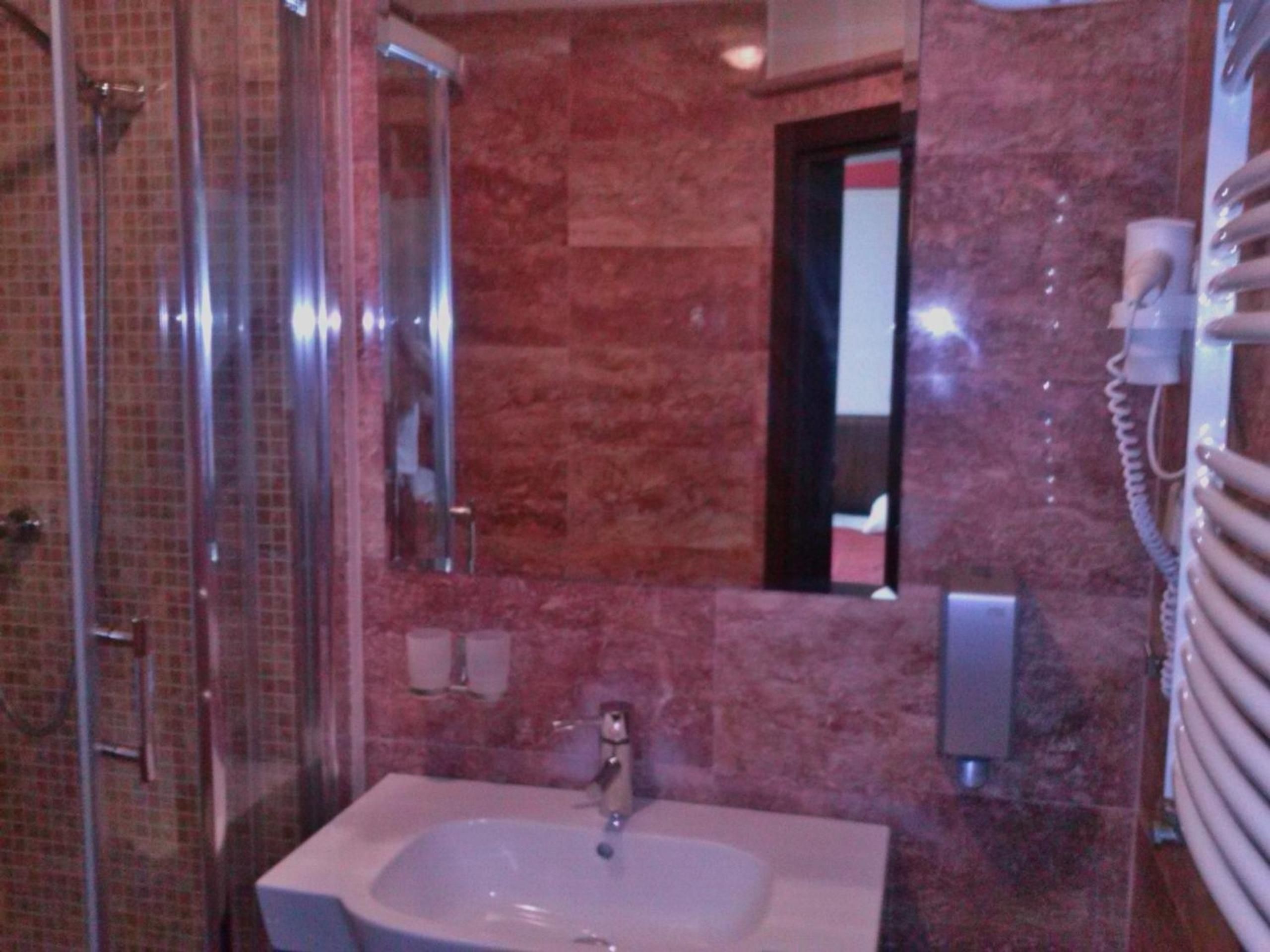 Ein Badezimmer mit Duschkabine aus Glas, Waschbecken und einem Spiegel sowie einem Telefon.