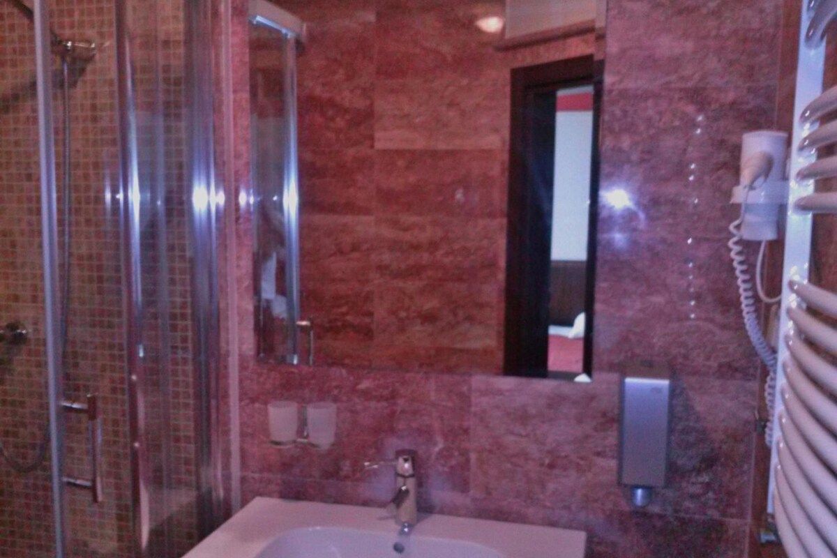 A bathroom with a glass shower enclosure, a sink with a mirror, and a telephone.