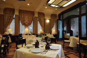 A restaurant with multiple tables set for dining, featuring white tablecloths and gold-toned cutlery. - Hotel Victoria (Wloclawek)