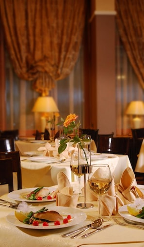 Una mesa de comedor dispuesta con platos, vasos y cubiertos, con un centro de rosas y una vela al fondo.