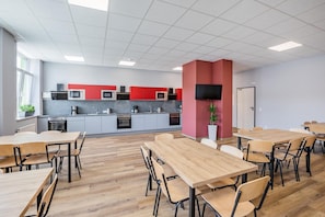 Una cocina moderna con armarios grises y rojos, un televisor de pantalla plana y una zona de comedor con mesas y sillas de madera.