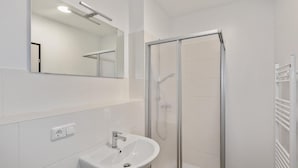 Un baño con un lavamanos blanco, un espejo y una ducha con mampara de vidrio.