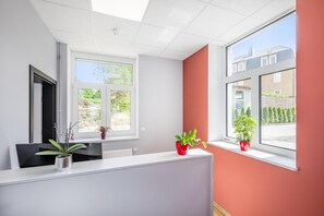 Un espacio de oficina moderno con un mostrador de recepción, dos ventanas que dan a una zona residencial y plantas en el alféizar.