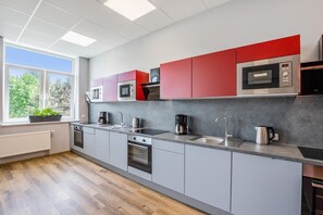 Una cocina moderna con armarios grises, armarios superiores rojos, electrodomésticos de acero inoxidable y un ventanal con vista a árboles.