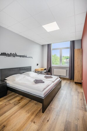 Habitación de hotel moderna con una cama grande, un escritorio, una silla y vistas al exterior a través de una ventana.