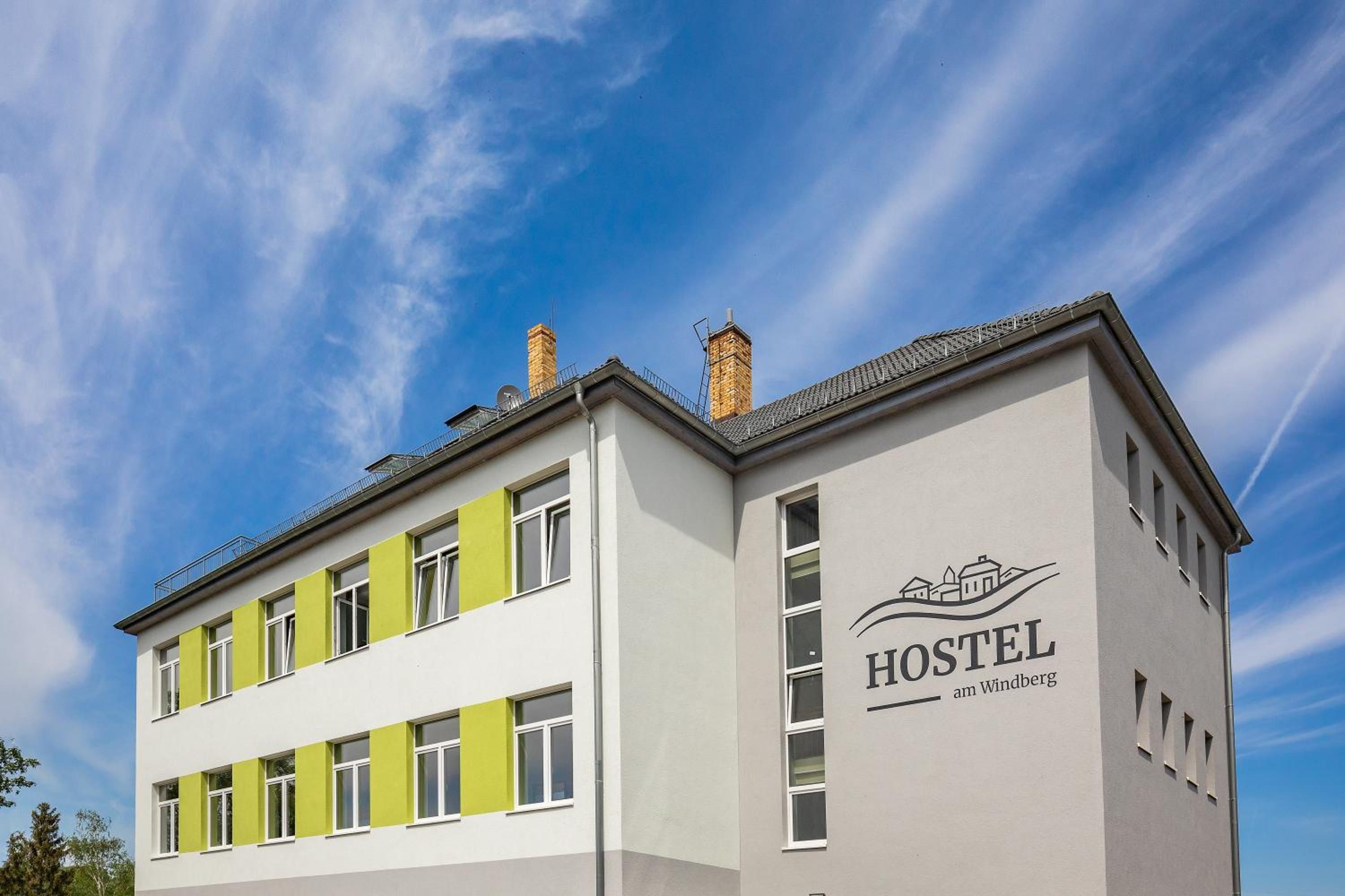 A hostel building with a modern design, featuring a prominent logo and the name 'HOSTEL am Windberg' on the facade.