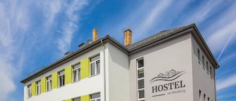 Un bâtiment d’auberge de jeunesse au design moderne, avec un logo bien visible et le nom « HOSTEL am Windberg » affiché sur la façade.
