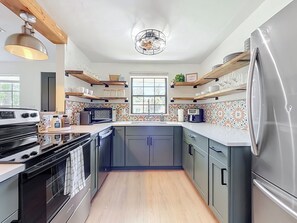 A modern kitchen with a built-in oven, a refrigerator, and wooden shelves above the counter. - NEW! Pet-Friendly Modern Cottage, Steps to Jax Beach (Jacksonville Beach)