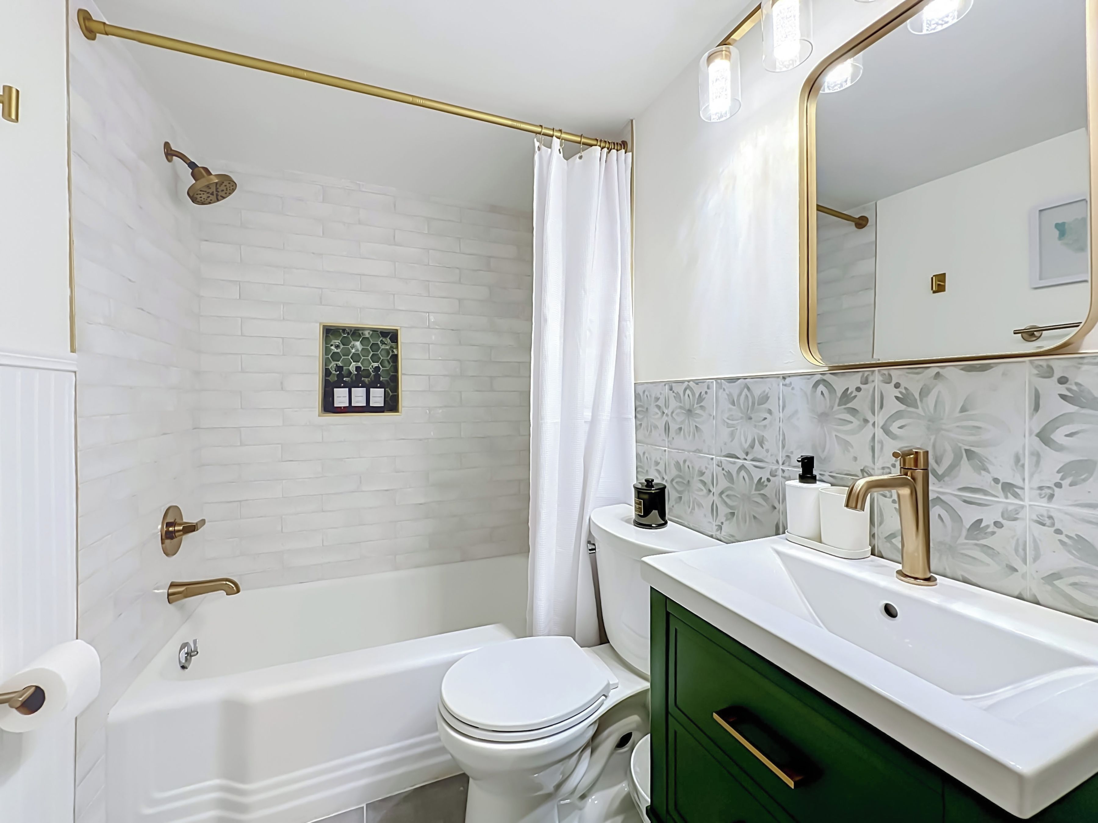 Ein Badezimmer mit Badewanne, Toilette und Waschbecken, mit einer Farbgestaltung in Weiß und Grün sowie einem beleuchteten Spiegel.