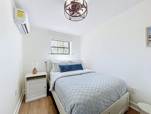A bedroom with a bed, bedside table, lamp, window, and ceiling fan. - NEW! Pet-Friendly Modern Cottage, Steps to Jax Beach (Jacksonville Beach)