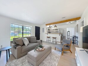 Un salon moderne comprenant un canapé, un pouf et un coin repas avec des chaises et une table.