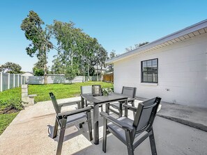 An outdoor patio with a table and chairs, a white building in the background, and a grassy area. - NEW! Pet-Friendly Modern Cottage, Steps to Jax Beach (Jacksonville Beach)