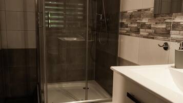 A modern bathroom with a glass-enclosed shower, a white vanity, and a tiled backsplash.