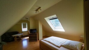 Una habitación pequeña con techo inclinado, una cama individual, un televisor y un ventanal.