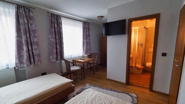 Habitación con dos camas, un escritorio con silla, televisor montado en la pared y zona de ducha.