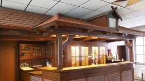 Una zona de bar con barra de madera, base de ladrillo, armarios de madera y techo con azulejos.