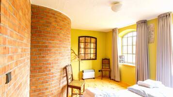 Ein Zimmer mit Backsteinwand, einem Bett, einem Sessel, einem Heizkörper und einem Fenster mit Vorhängen.