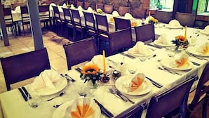 Comedor con mesas dispuestas para varios comensales, con manteles blancos, cubiertos ordenados y centros de mesa con flores.