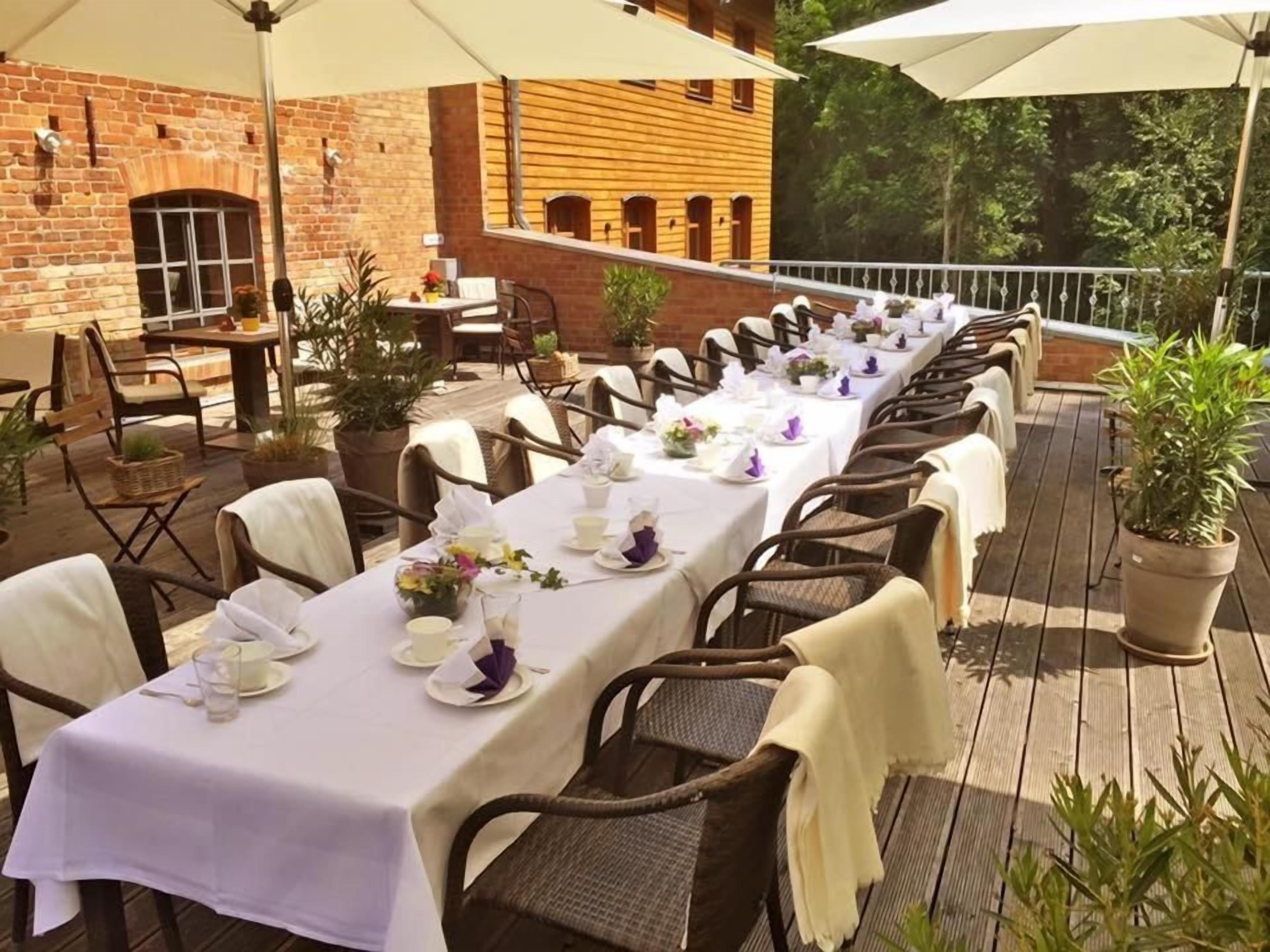 A long dining table set outdoors with chairs, umbrellas, and potted plants.