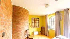 Una habitación con pared de ladrillo, cama, silla, radiador y ventana con cortinas.