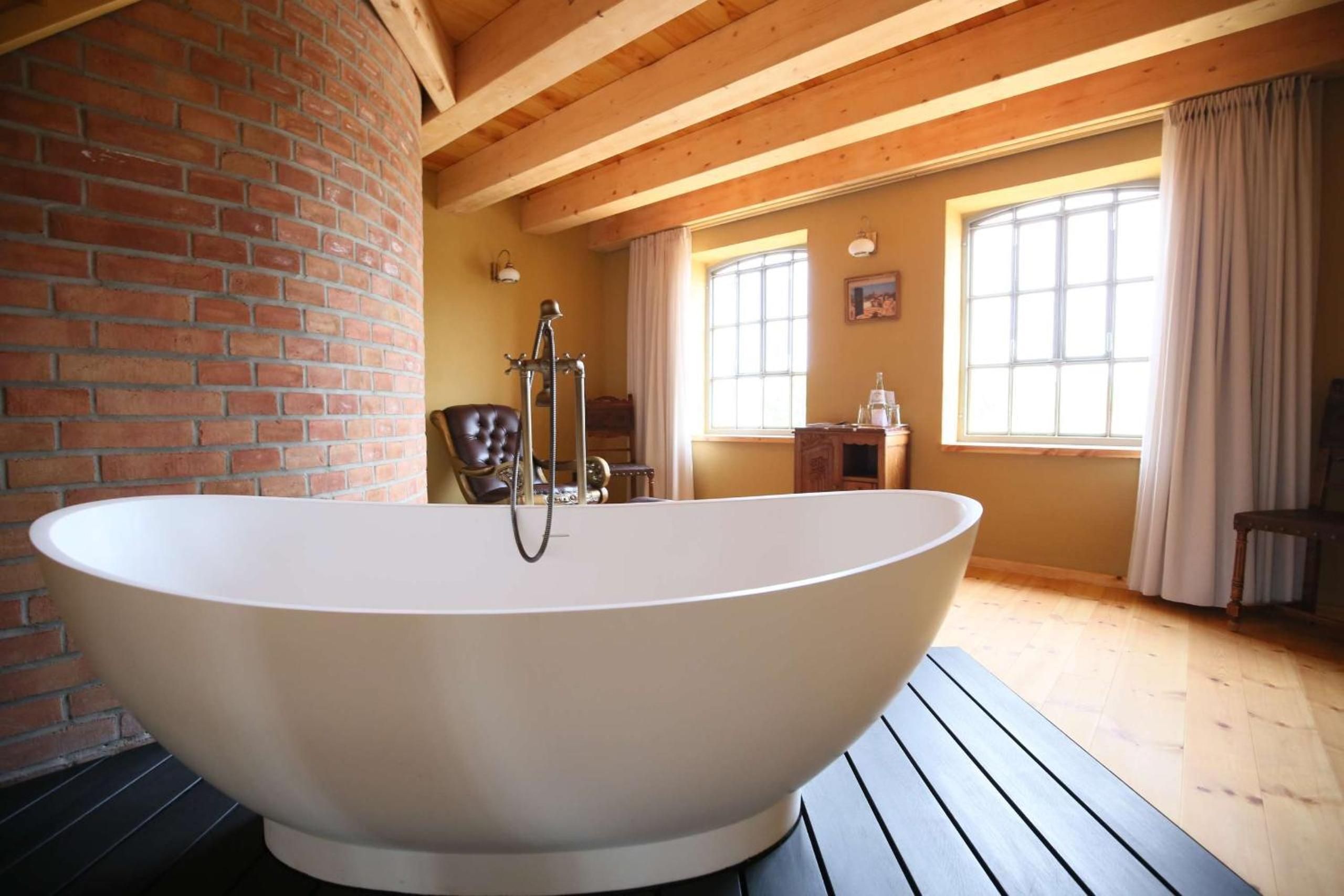 Eine große, freistehende Badewanne in einem Raum mit Holzbalken und Backsteinwänden.