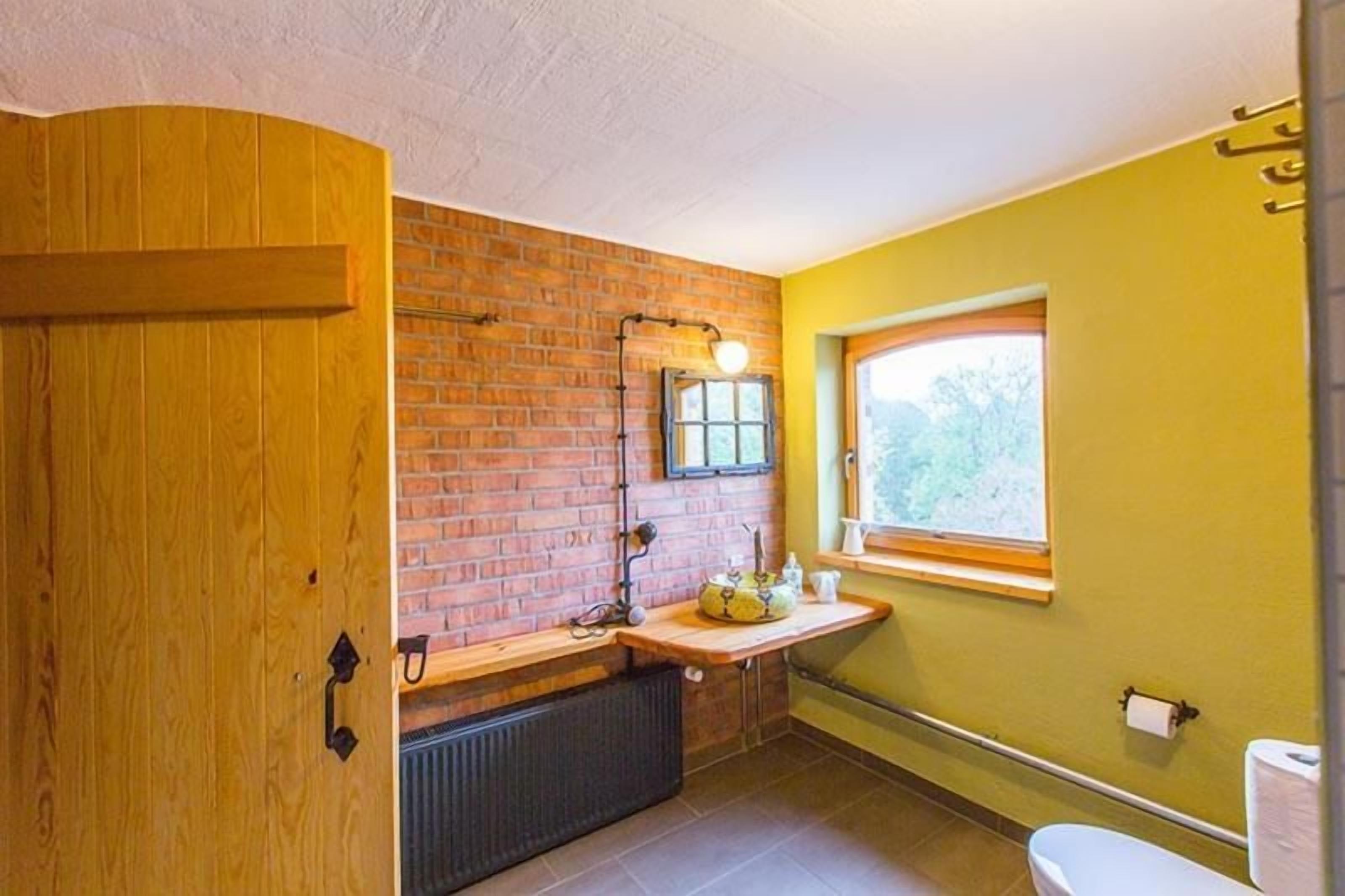 Ein Badezimmer mit Holztür, Backsteinwand, Fenster und Waschbecken.