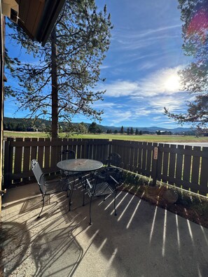 Eine Terrasse mit Tisch und Stühlen, ein Holzzaun und der Blick auf eine grüne Landschaft mit Bäumen und Hügeln.