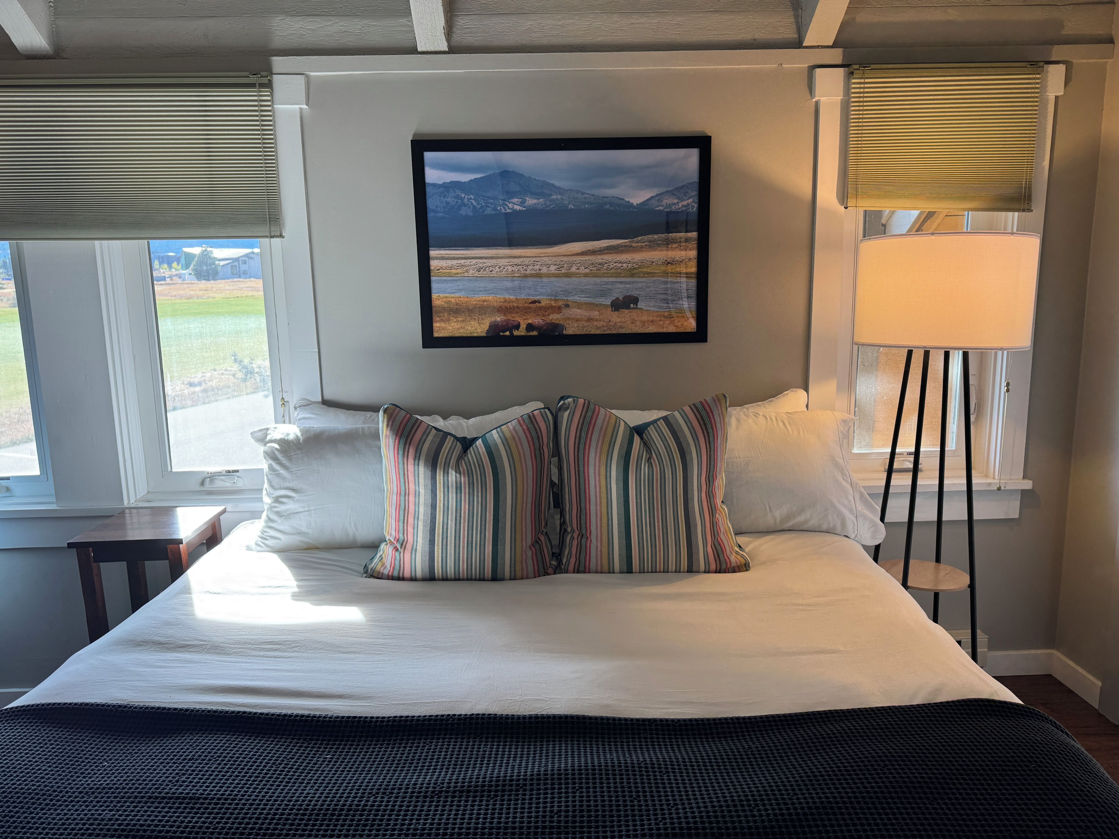 A bed with a view of a mountainous landscape through a window, a bedside lamp, and a framed picture on the wall.