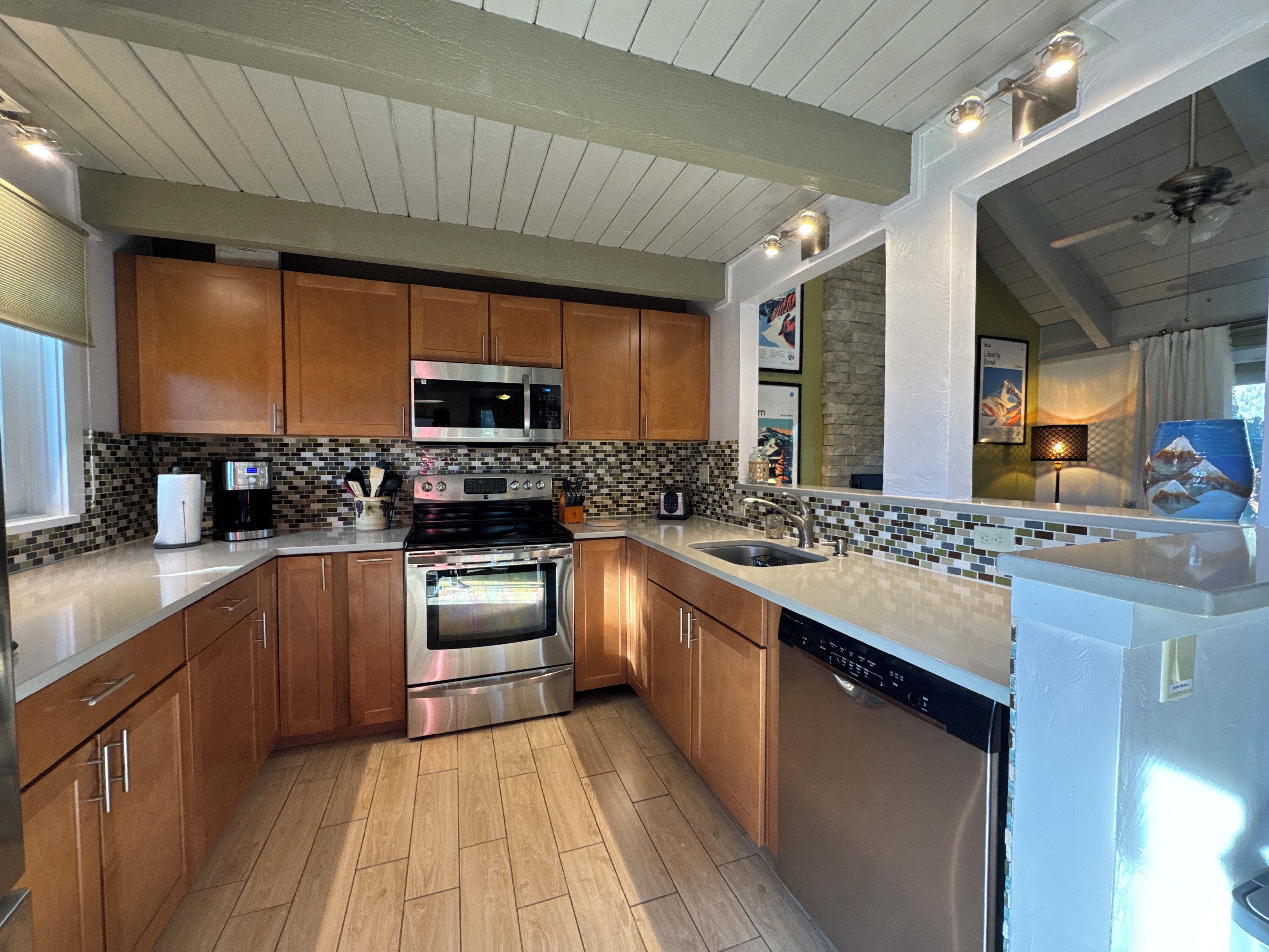 Una cocina moderna con gabinetes de madera, electrodomésticos de acero inoxidable, salpicadero de azulejos y lavavajillas.