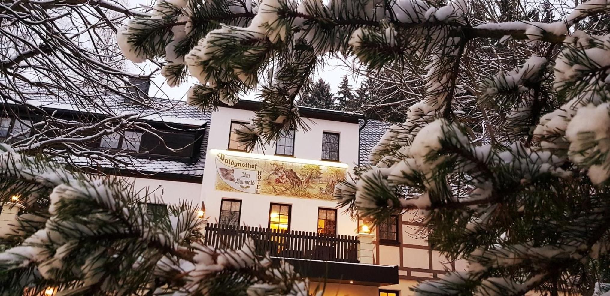 Ein Hotelgebäude mit sichtbarem Schild, einem Balkon und schneebedeckten Ästen im Vordergrund.