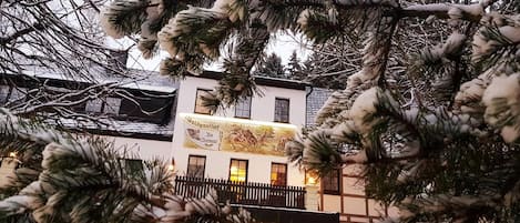 Un edificio de hotel con un letrero visible, un balcón y ramas cubiertas de nieve al frente.