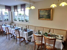 Uma sala de jantar com mesas preparadas para o serviço, cadeiras e um quadro na parede.