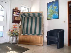 Una habitación con un banco a rayas, un sillón negro, un mapa en la pared y un tablón de anuncios con varios avisos.