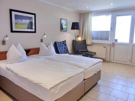 Habitación de hotel con cama doble, dos mesitas de noche, una silla, una lámpara de pie y una ventana con cortinas.