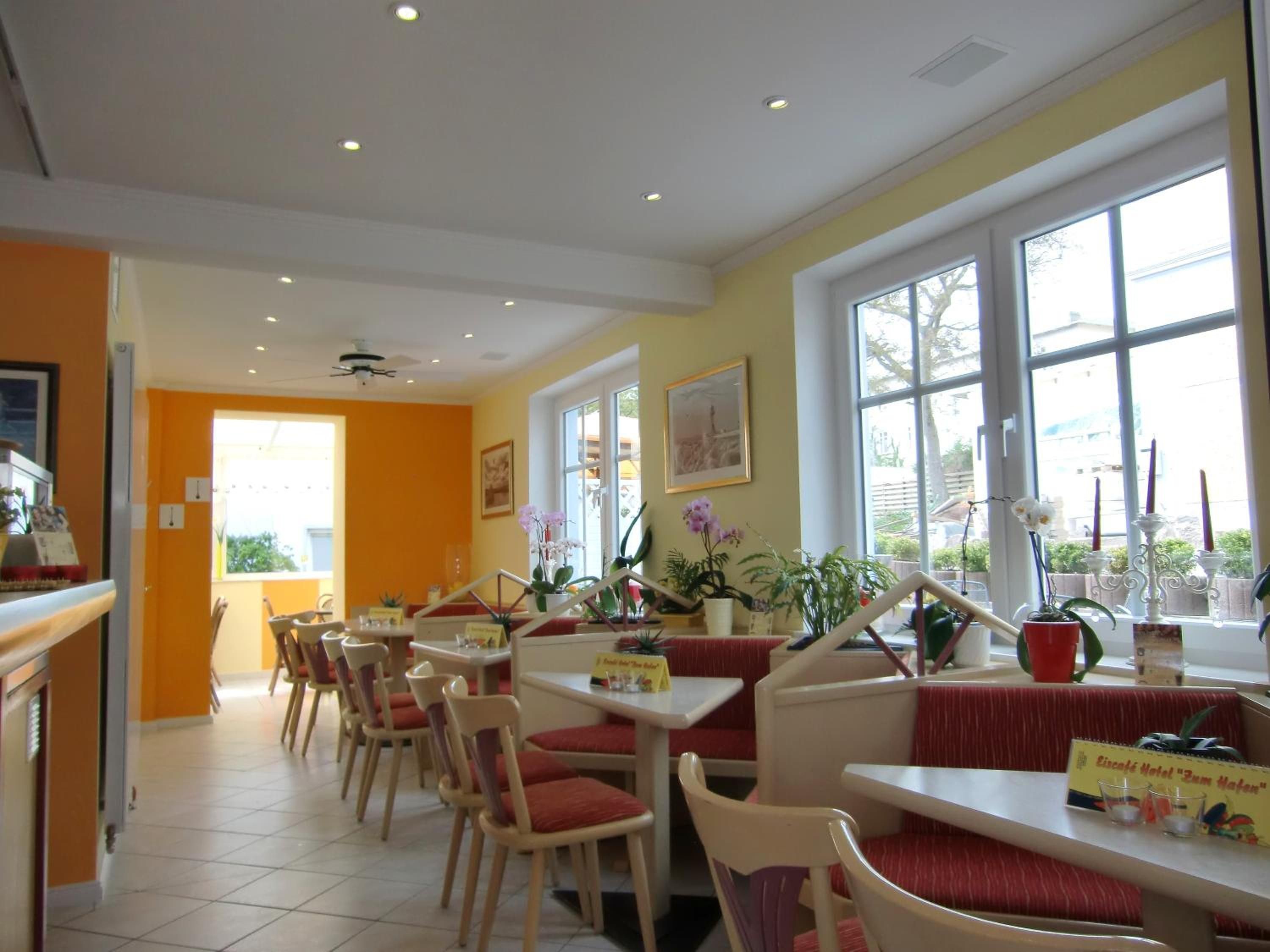 Un restaurante con cabinas y mesas, ventanas amplias y plantas de interior.