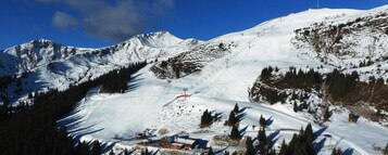 Montaña nevada con pistas de esquí, una cabaña pequeña y un cielo azul despejado.