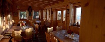 Interior de una cabaña de madera con comedor, varias ventanas y vistas al exterior.