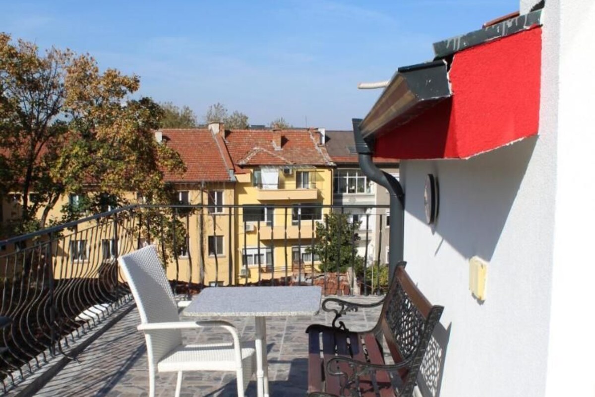 A terrace with stone flooring, a white chair, a wooden bench, and a red awning.
