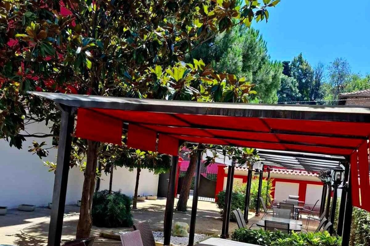 An outdoor patio with a red pergola, wicker furniture, and a view of the surrounding garden.