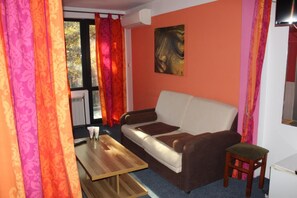 A living room with a sofa, a small table, a chair, and a painting on the wall. - Hotel Color (Asenovgrad)