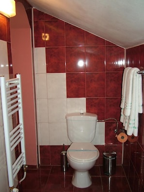 A bathroom with a toilet, a towel rack with towels, a radiator, and a trash bin. - Hotel Color (Asenovgrad)